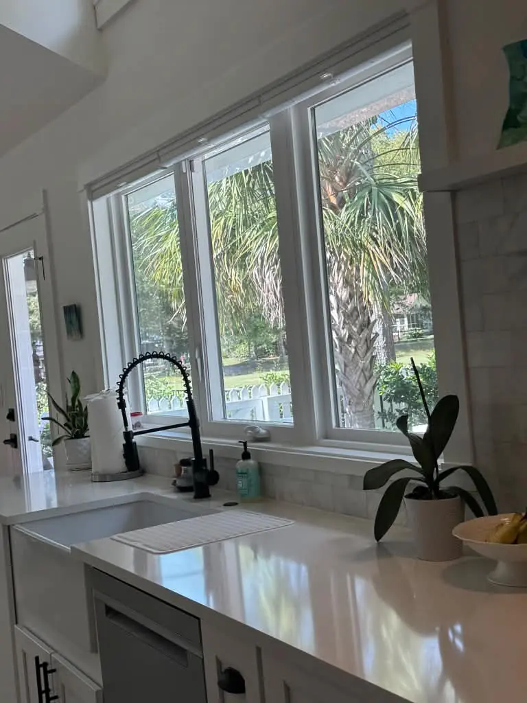 Clean kitchen sink and white countertop beside a sunny window